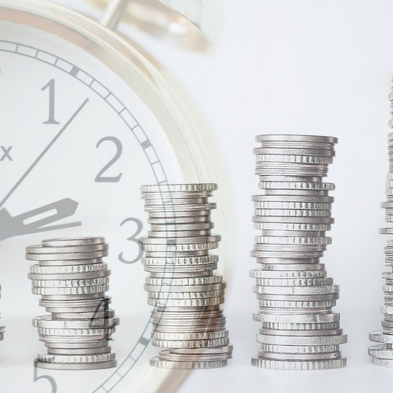 clock faded with stacks of coins in front of it