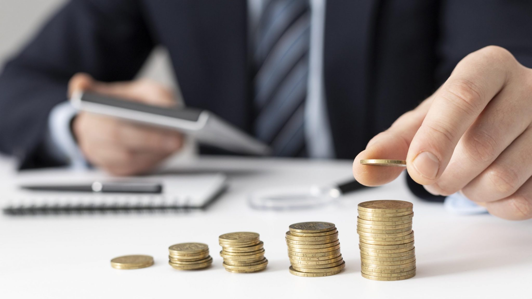 stacks of coins incrementing in size with last stack having coin added to it by hand